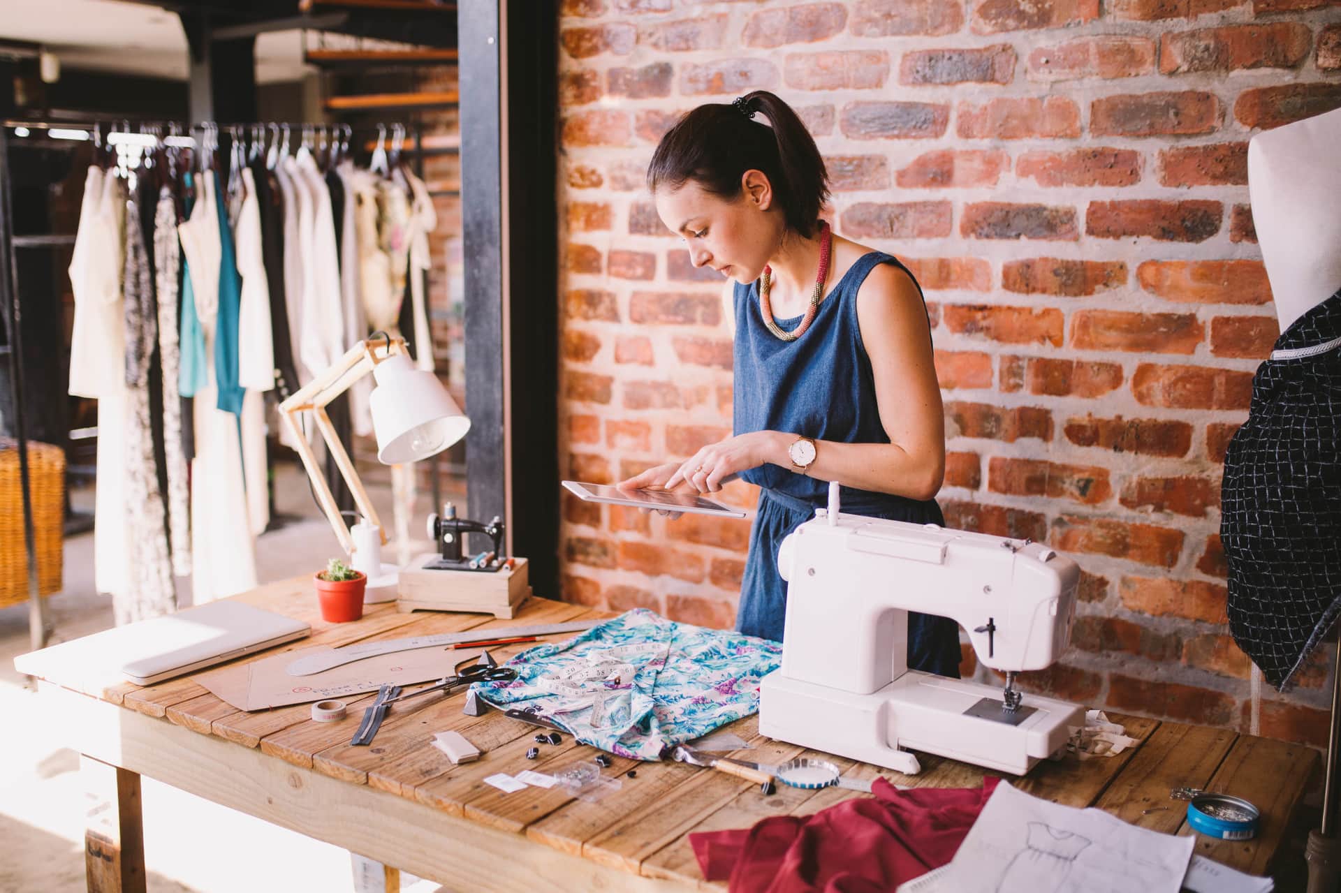 Fashion designer working with textiles in her boutique and ordering supplies on a digital tablet